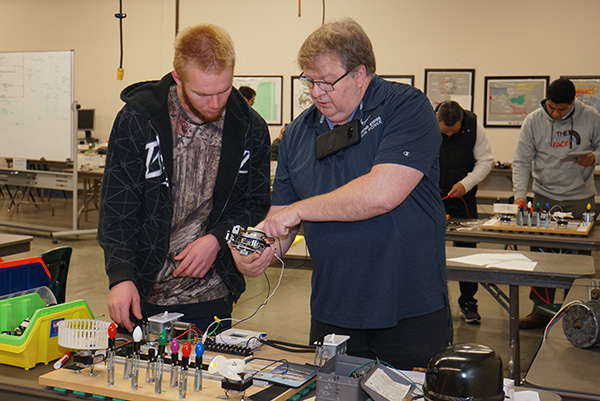 a teacher displaying an electronic device to an adult male student in a classroom