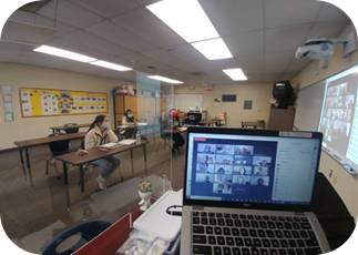 Photo of the classroom set up with a laptop in front, students on the side, and an electronic whiteboard facing the students.