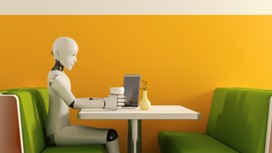 Robot sitting behind a table with a laptop