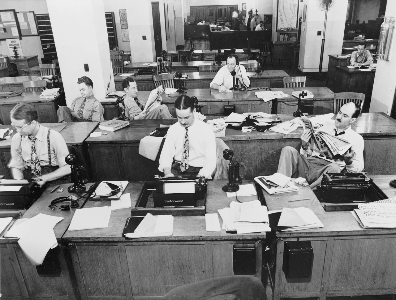 Workers using typewriters and phones with cords. Old technology.