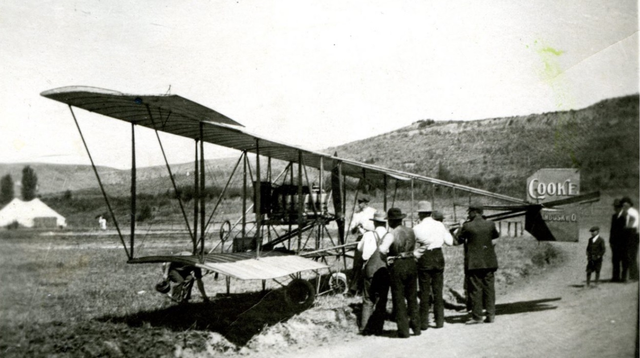 Men stand around and look at a biplane in a field.